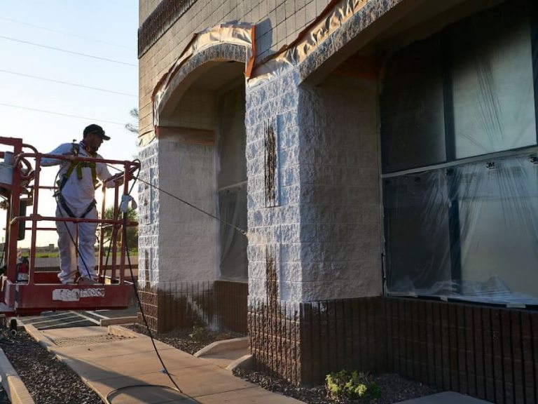 A contractor spray painting a stone facade during a professional retail store painting project