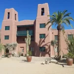 A building with a fresh coat of paint, surrounded by palm trees and lush plants.