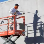 Painter using a lift to spray paint on the exterior of a building.