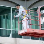 Painter on a lift spraying paint on a building's exterior.