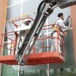 Painters on a lift preparing windows for repainting the exterior of a building, ensuring meticulous preparation and attention to detail.