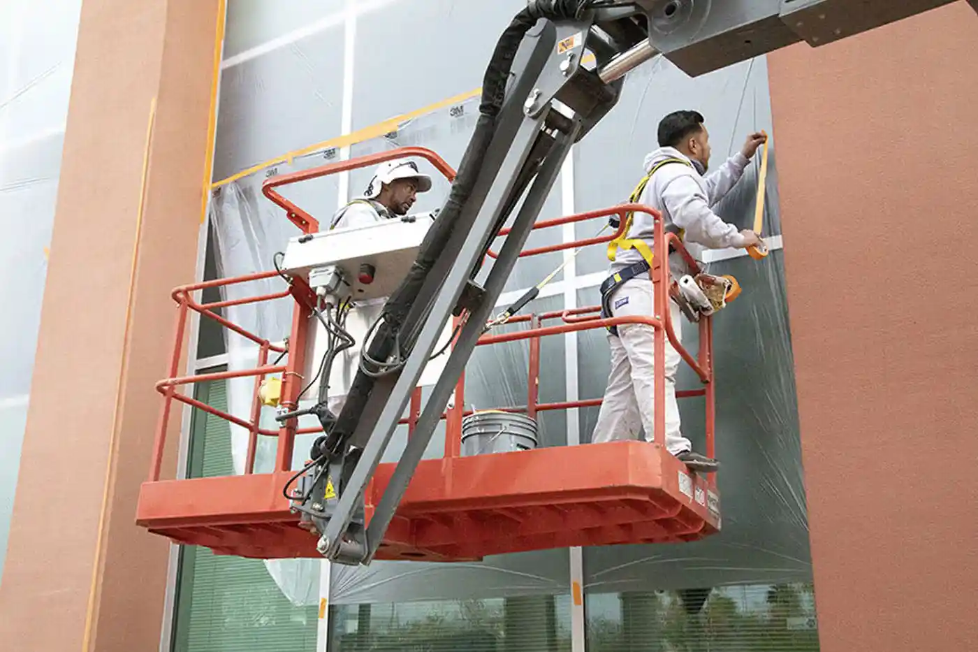 Painters on a lift preparing windows for repainting the exterior of a building, ensuring meticulous preparation and attention to detail.