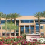 A commercial building surrounded by trees and flowers in the foreground, blending urban architecture with natural landscaping.