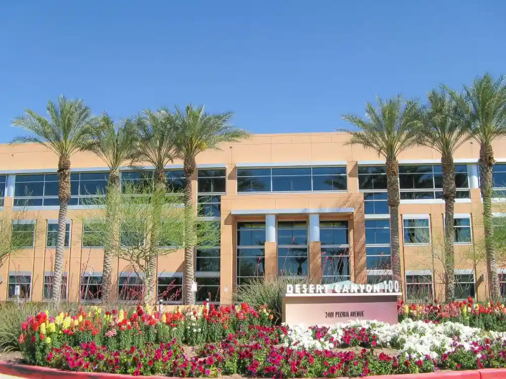 A commercial building surrounded by trees and flowers in the foreground, blending urban architecture with natural landscaping.