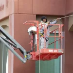 Painter using a paint sprayer to evenly coat a wall in fresh white paint, with focused concentration on achieving smooth coverage.
