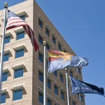 Three flags mounted on separate poles, waving in the breeze against a clear sky.