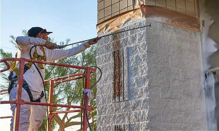 Worker applying protective coating to concrete building exterior